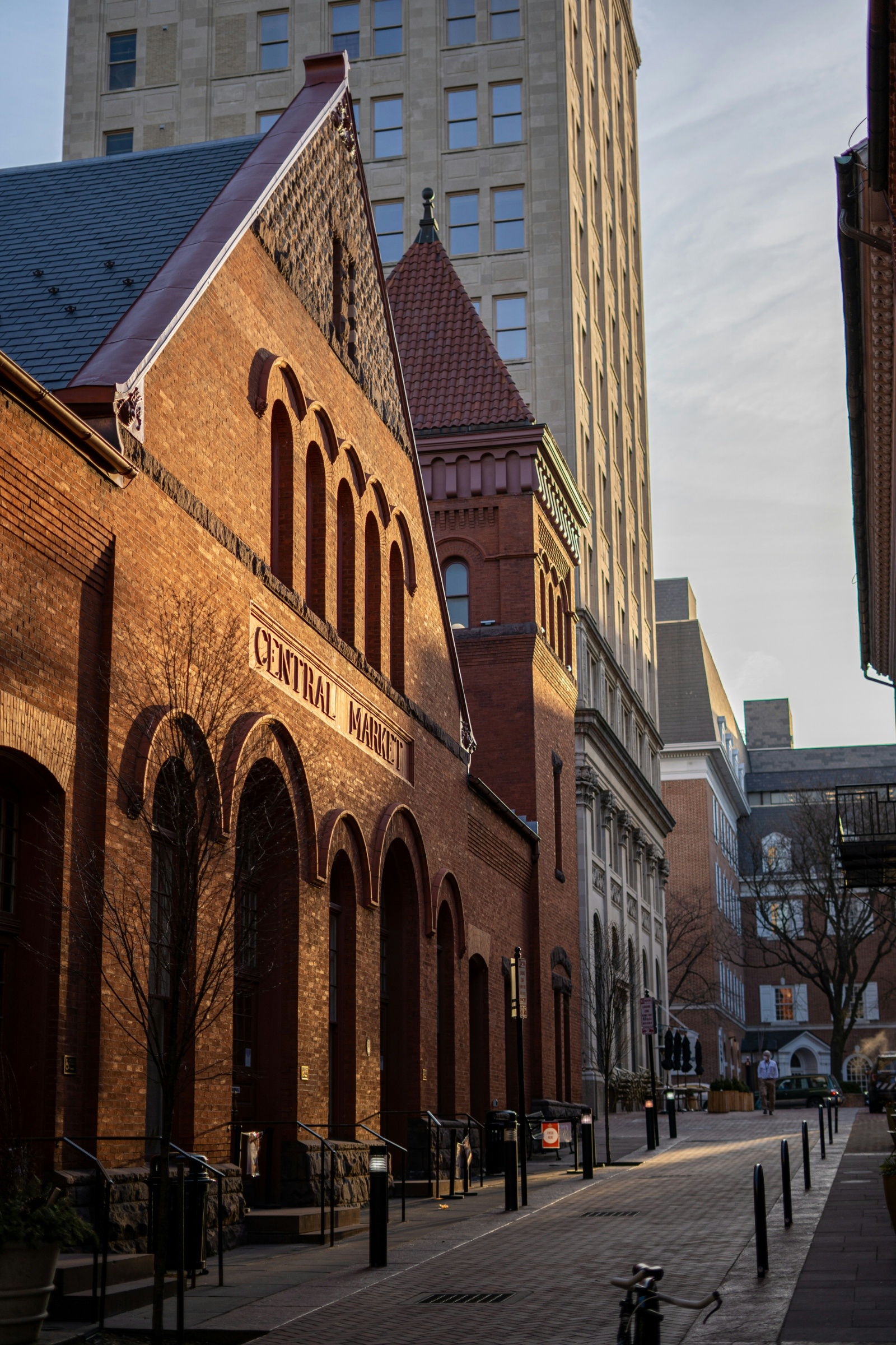 A sunlit street with a historic brick building in Lancaster, Pennsylvania labeled "Central Market." Tall modern buildings rise behind, creating a contrast of old and new architecture.