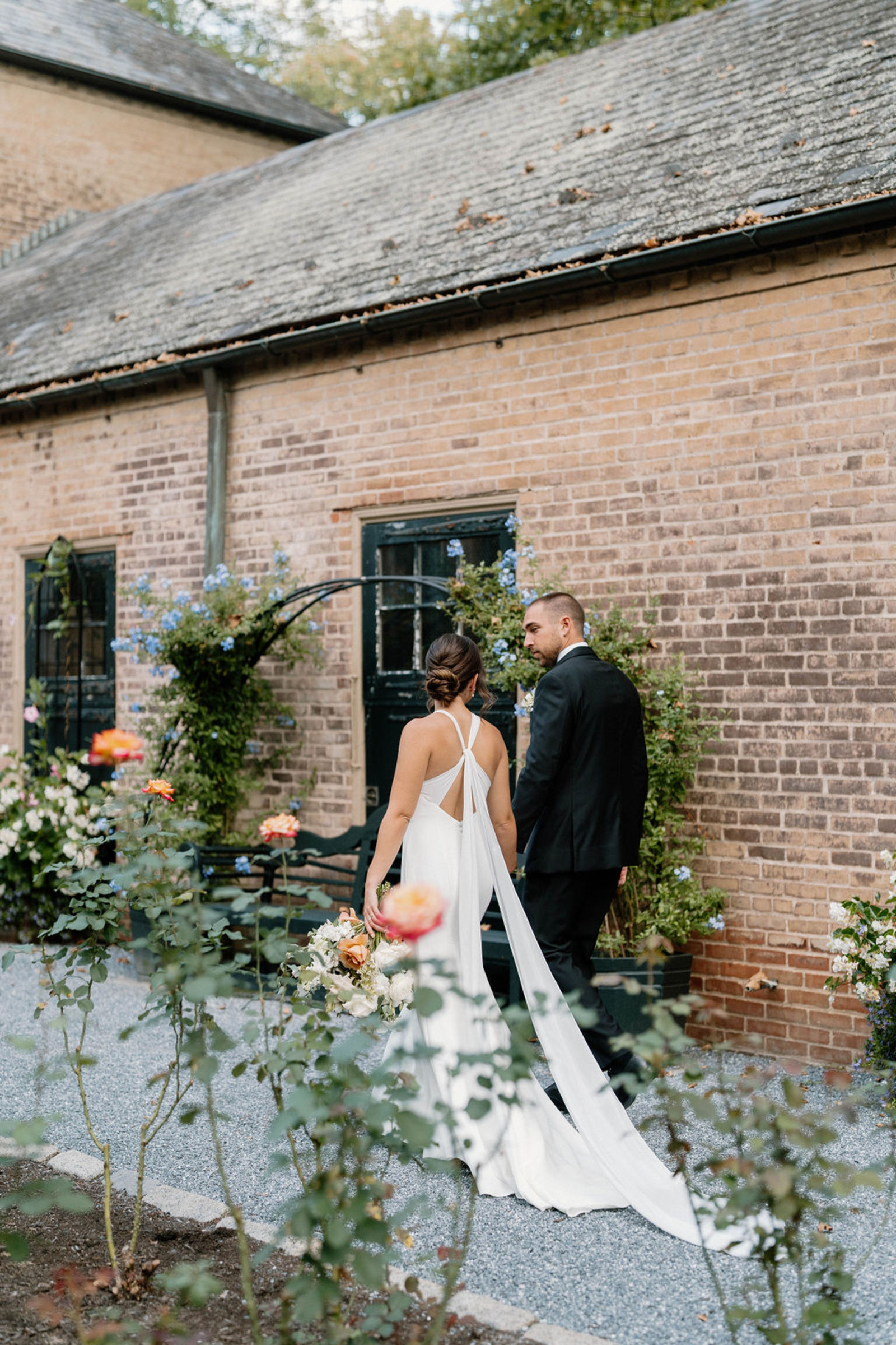 Bride and groom walking through a courtyard garden with brick buildings and flowers at a Lancaster PA wedding venue