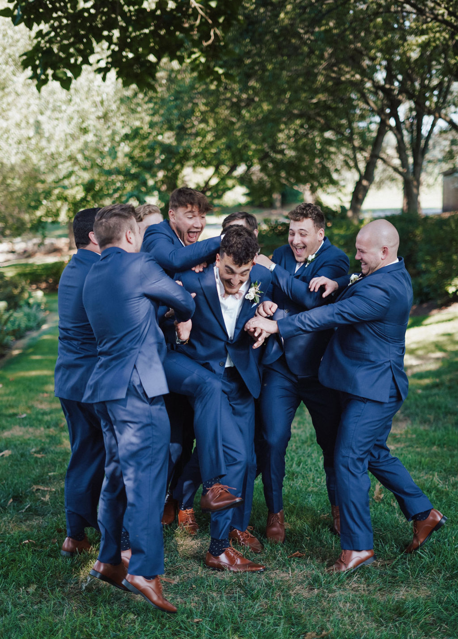 Central PA groomsmen in navy suits surround the groom and playfully rough-house with him
