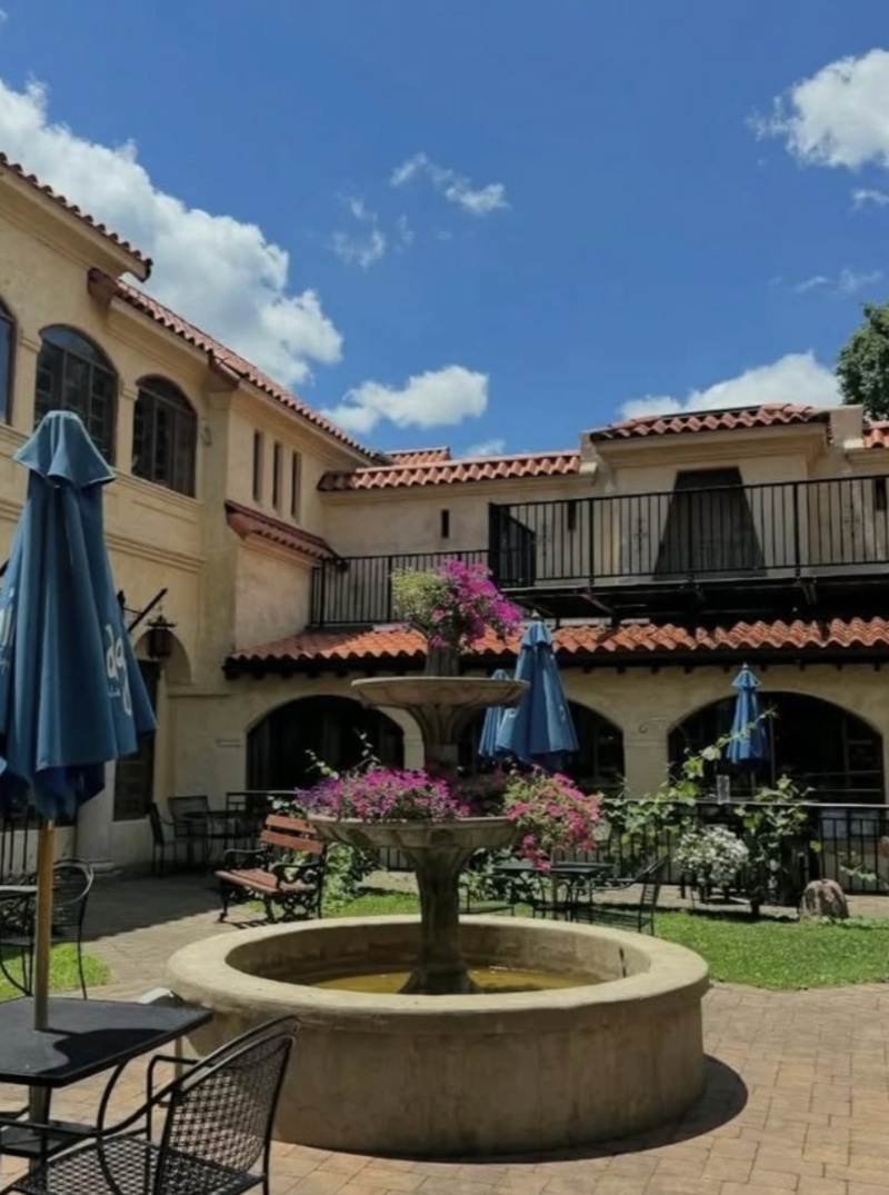 Outdoor courtyard at El Serrano in Lancaster, PA, featuring a central fountain, patio seating, colorful flowers, and Mediterranean-style architecture.