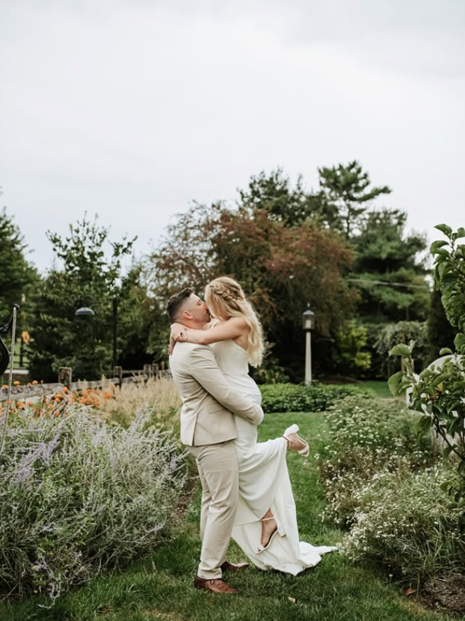 Bride and groom embracing on a garden path surrounded by greenery and flowers at a Lancaster PA wedding venue