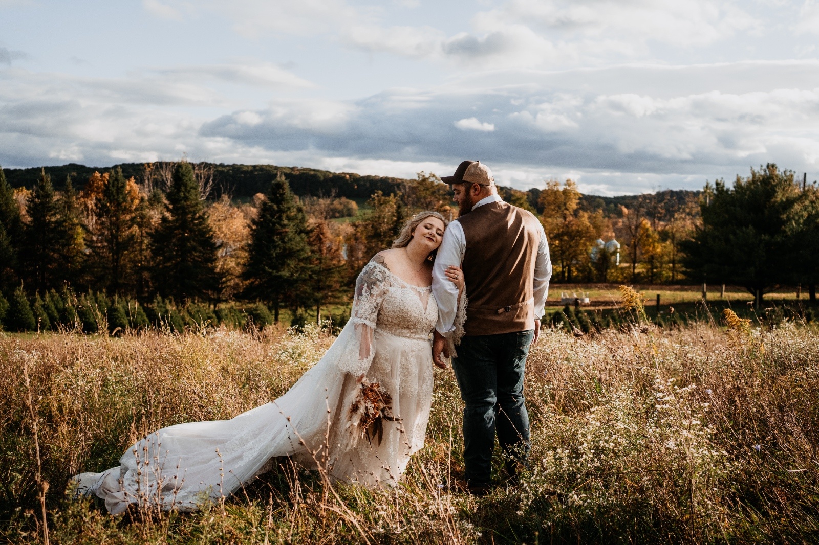 Couple holds hands during a golden-hour engagement shoot surrounded by trees, captured with a warm, moody style.