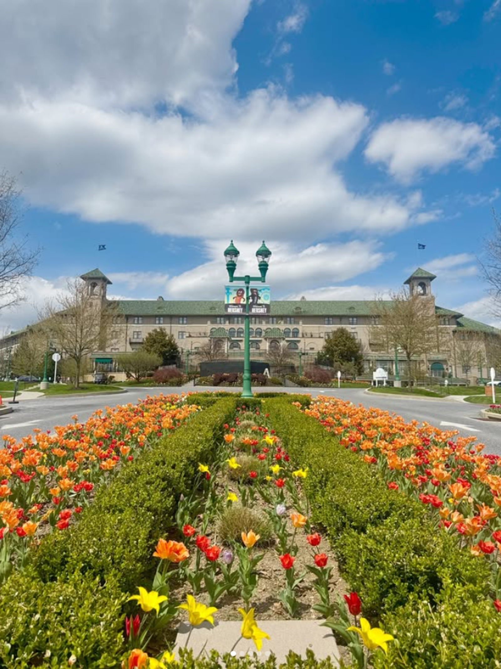 Colorful spring tulips line the entrance to The Hotel Hershey under a bright blue sky with large white clouds in Hershey, Pennsylvania.