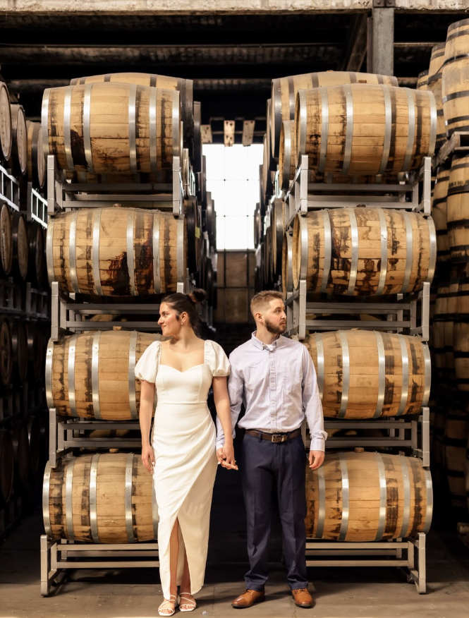 The Hidden Still in Hershey Couple walking between bourbon barrels inside The Hidden Still in Hershey, Pennsylvania, a unique rehearsal dinner restaurant and distillery.