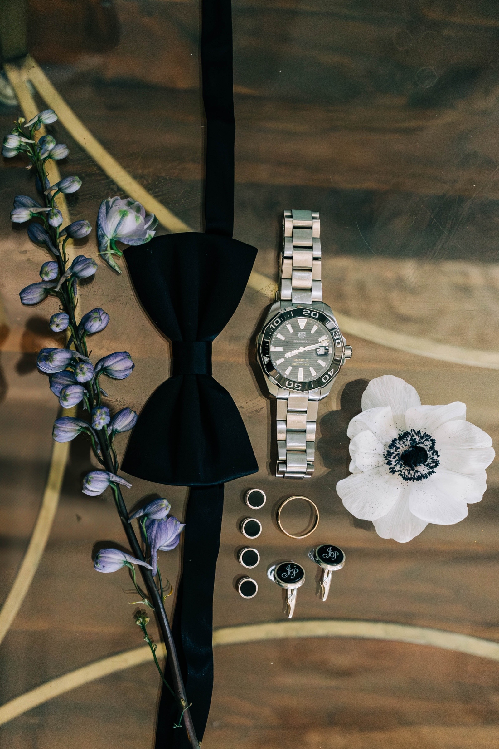 Groom Wedding Flat Lay with Watch, Bow Tie, and Cufflinks Groom wedding flat lay featuring black bow tie, watch, cufflinks, and boutonniere styled with rings and florals.