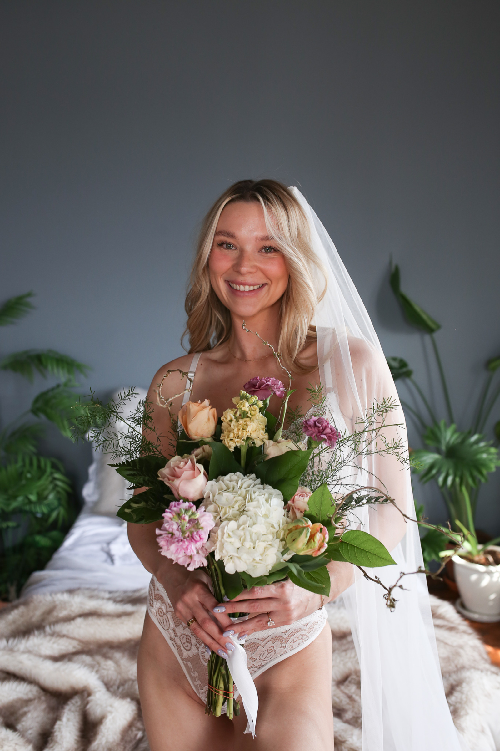 Smiling bride holding a pastel bouquet and wearing a veil during her empowering bridal boudoir photoshoot with Eileen C. Wenger Photography at Leaf & Loft Studio in Lancaster, PA.