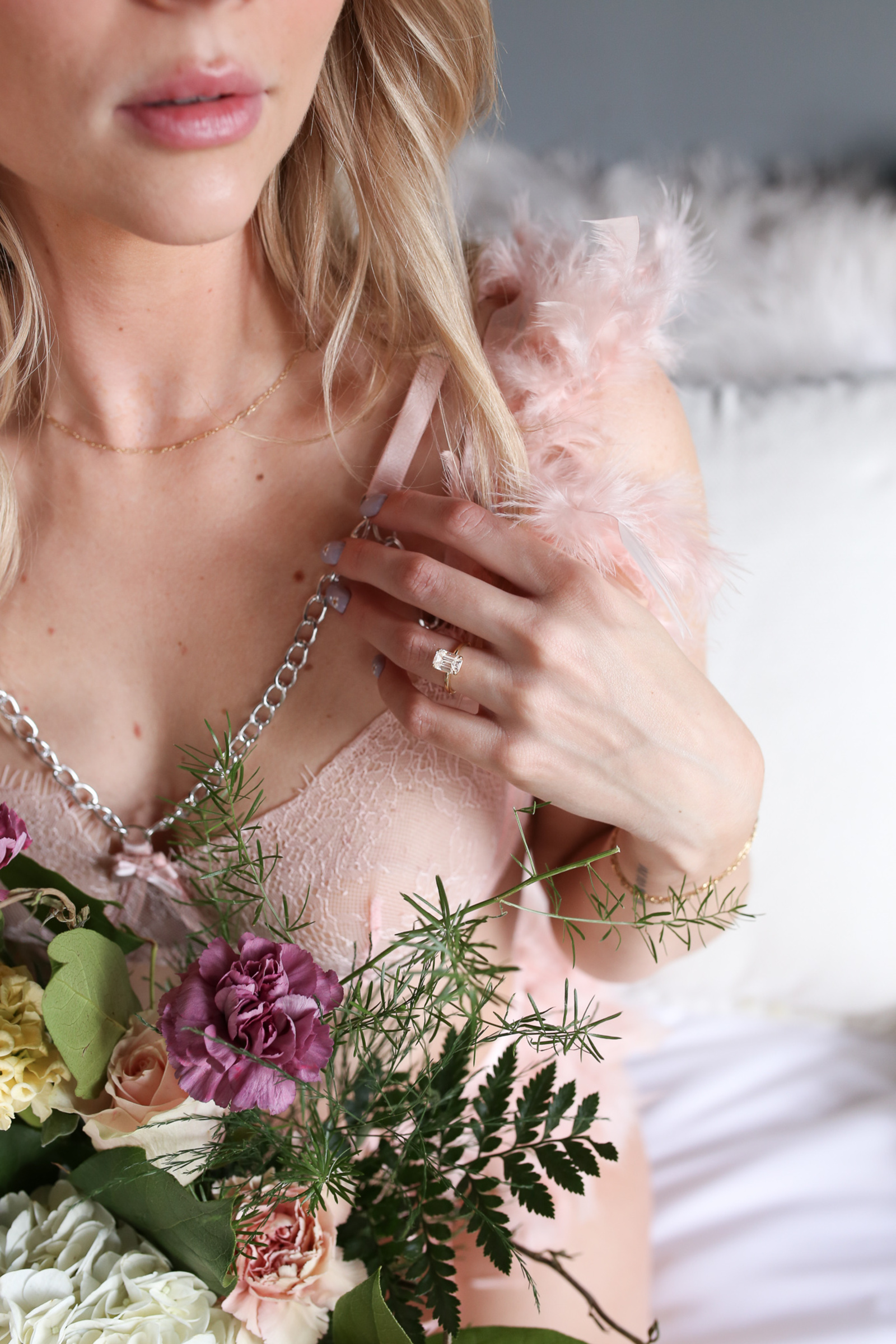 Close-up detail of a bride’s hand showcasing her engagement ring and soft pink lace lingerie, surrounded by delicate florals during a romantic bridal boudoir session with Eileen C. Wenger Photography in Lancaster, Pennsylvania.
