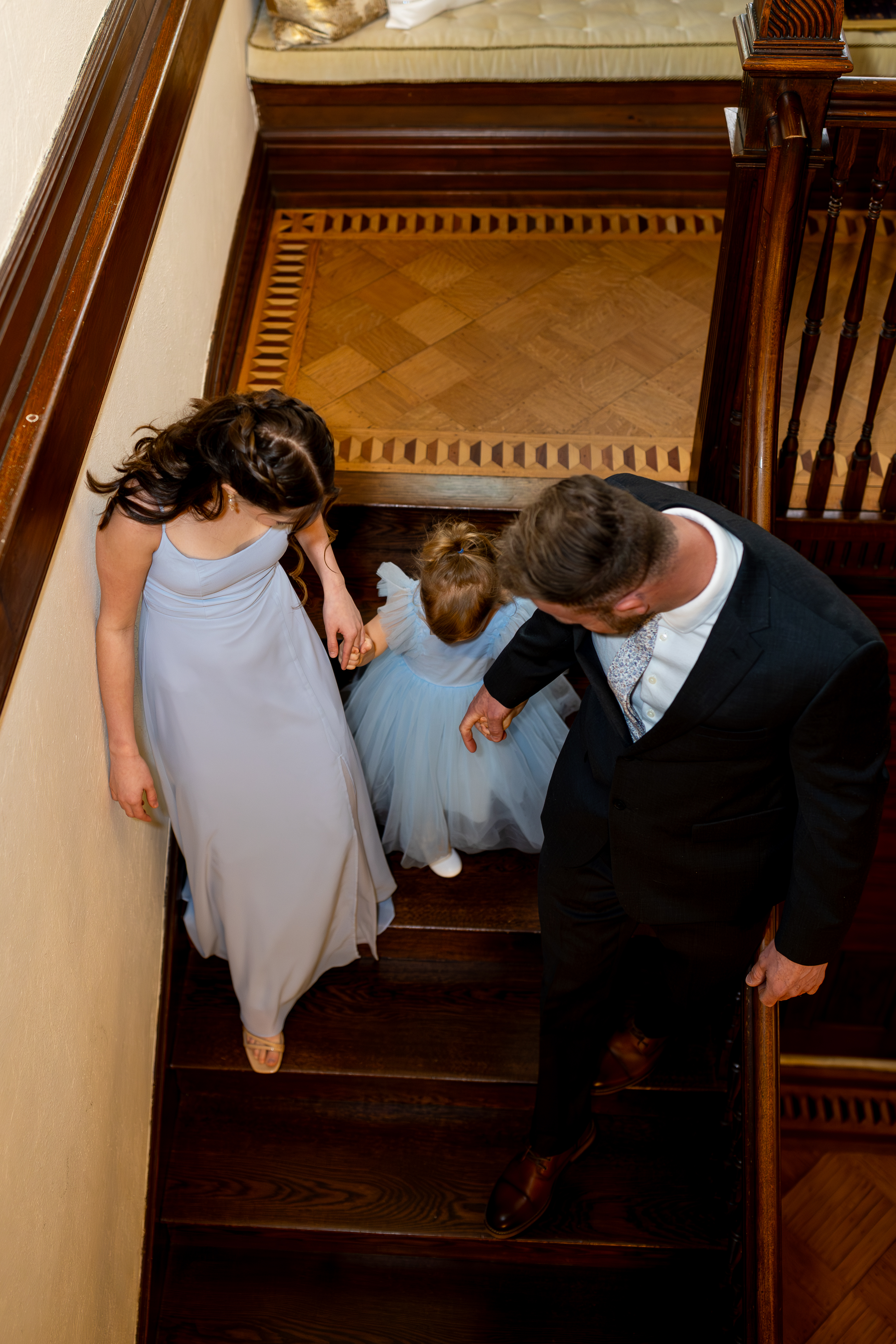 Bride's daughters and groom walk down a historic staircase together during a family-focused Pennsylvania elopement.