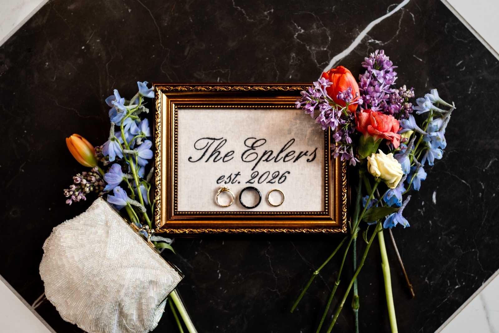 Wedding Flat Lay with Rings, Vintage Purse, and Florals Wedding flat lay featuring gold frame with rings, vintage beaded purse, and colorful florals styled on a marble surface.