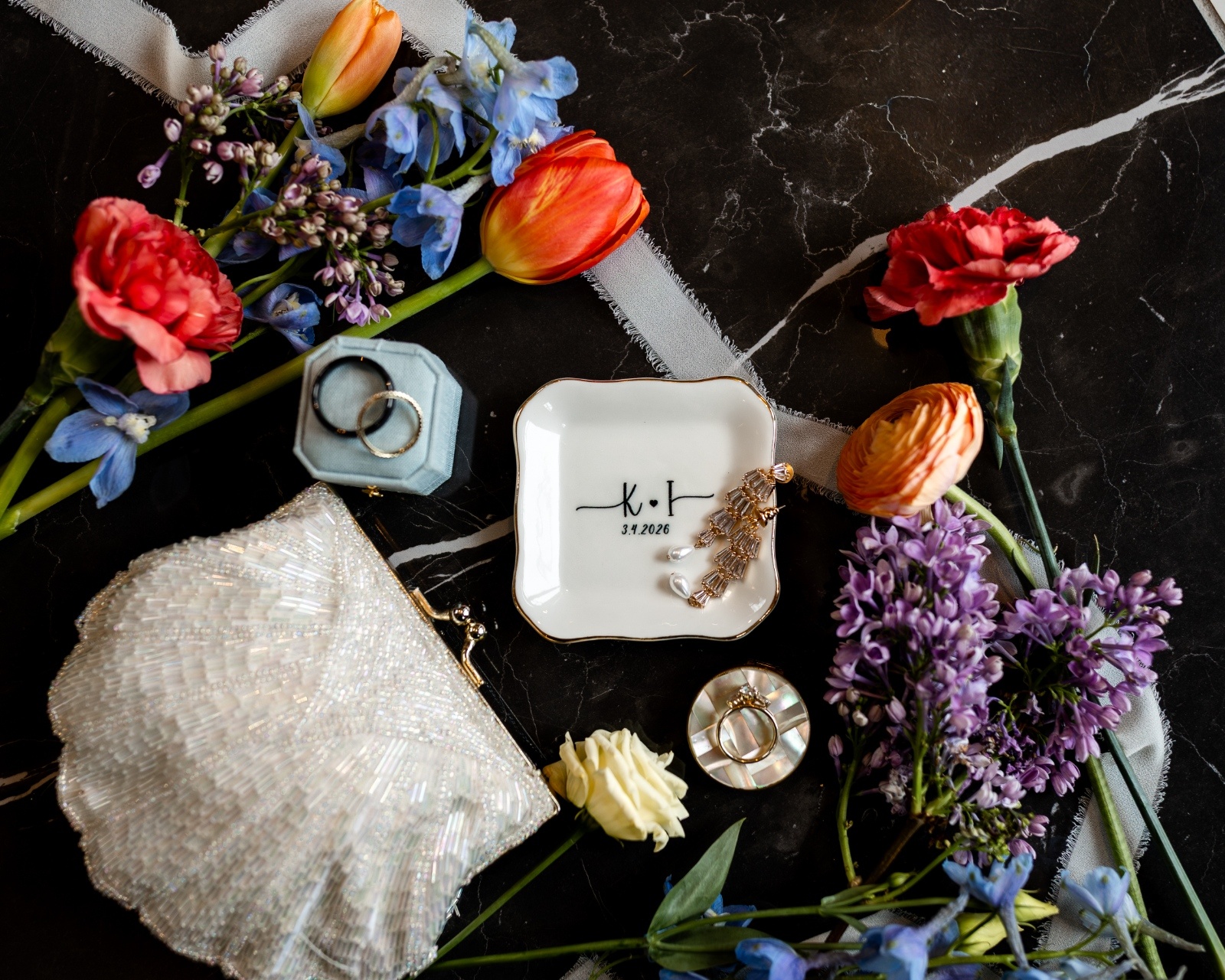 Wedding Flat Lay with Ring Box, Jewelry Dish, and Florals Wedding flat lay with blue velvet ring box, jewelry dish, vintage purse, ribbon, and colorful florals styled on marble.