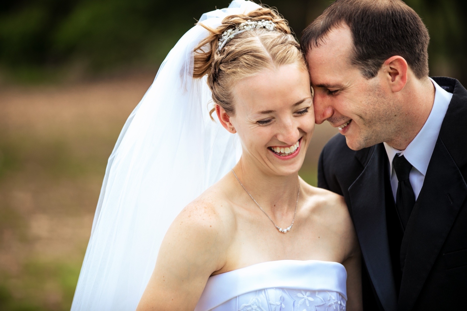 Bride laughs as the groom leans in close during a candid wedding portrait that captures their genuine connection and happiness.