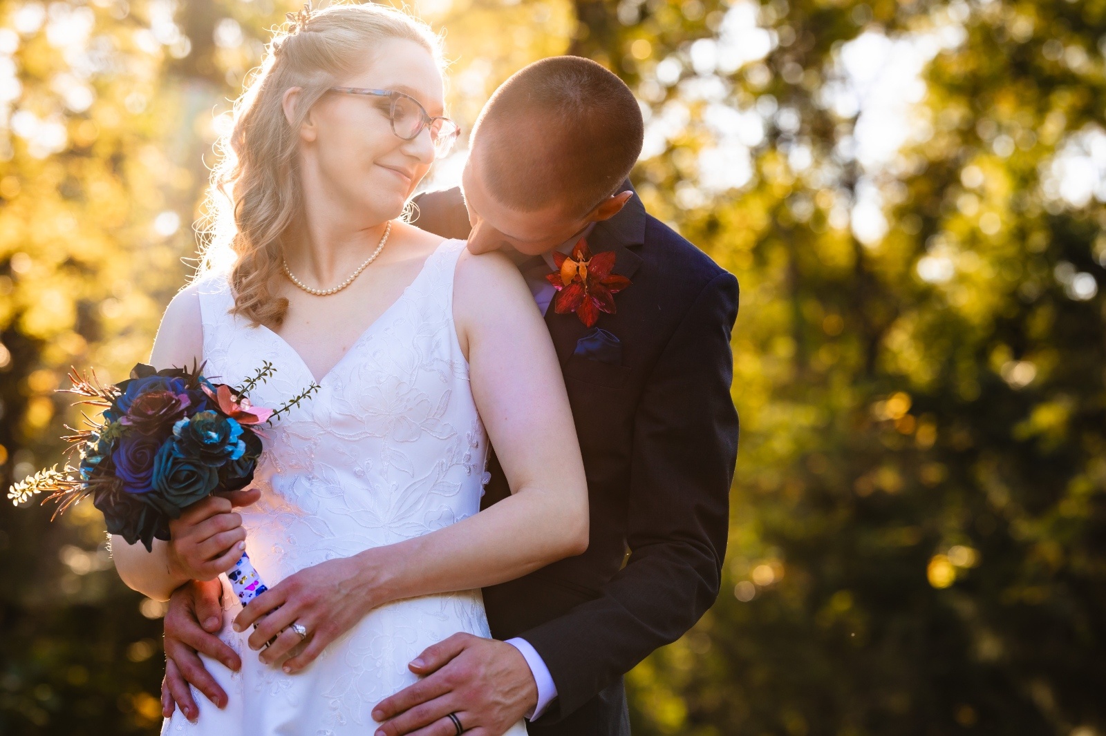 Groom embraces the bride from behind during a golden hour wedding portrait as she smiles and holds a colorful bouquet outdoors in Pennsylvania.