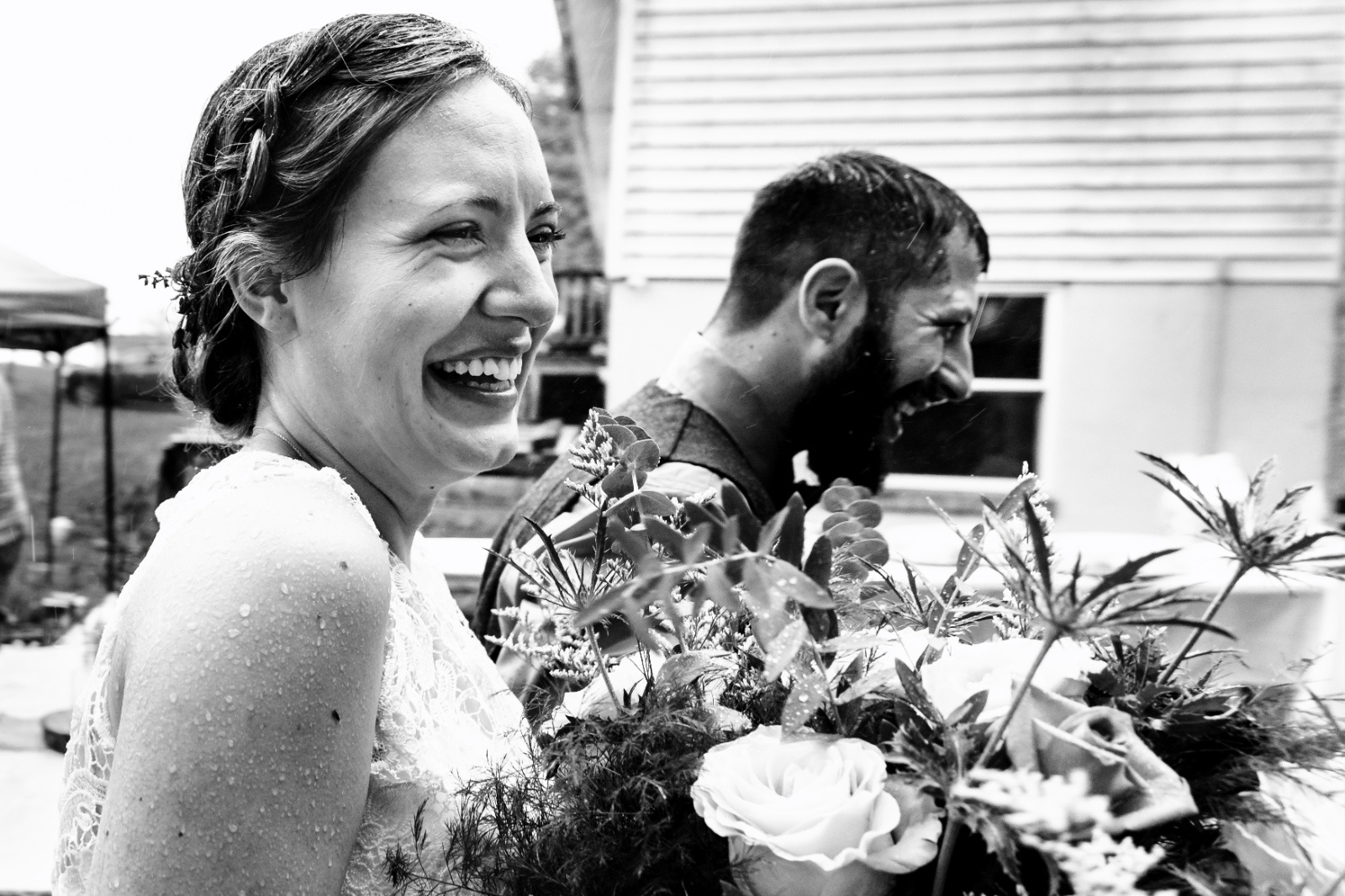 Bride laughs in the rain beside her groom during a backyard wedding, capturing a candid and joyful moment.