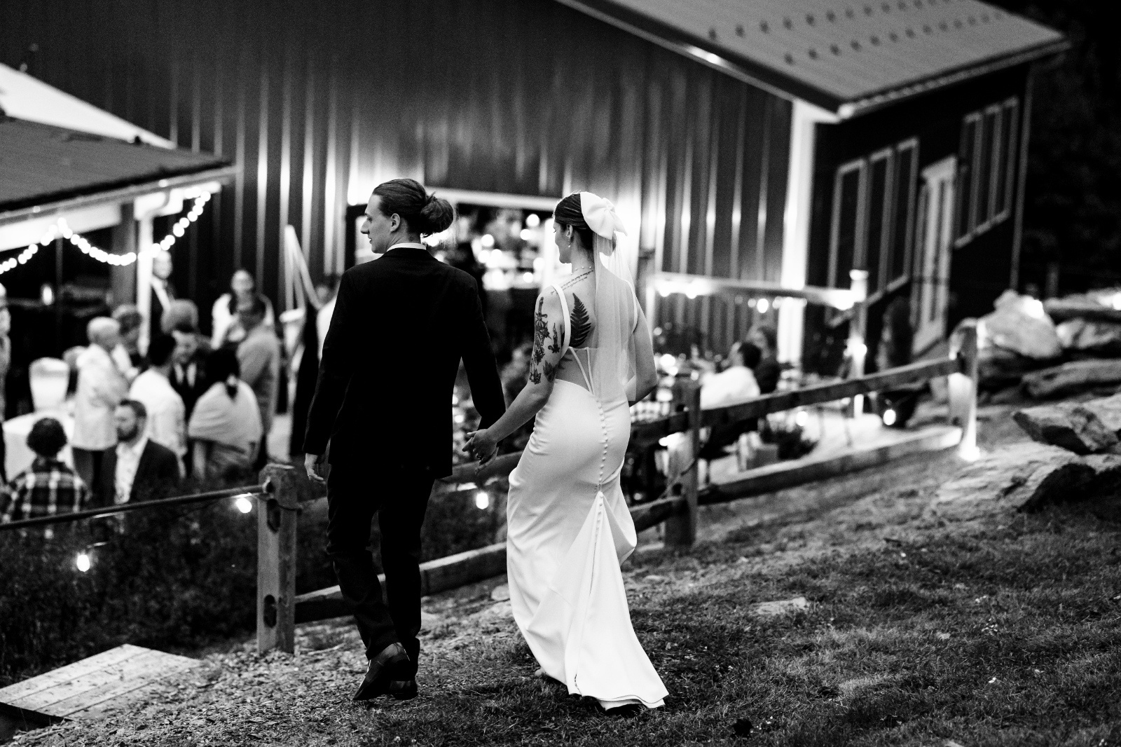 Newly married couple walks hand in hand toward their evening wedding reception in a timeless black and white photograph.