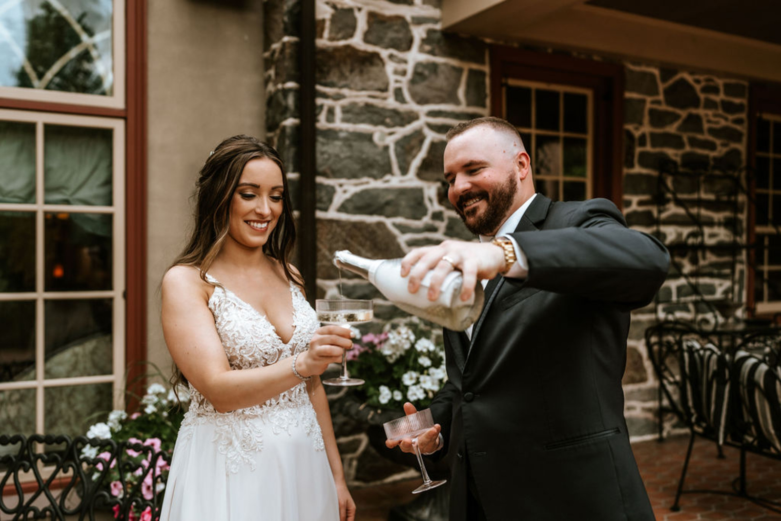 Groom pours champagne into the bride’s glass as they celebrate their marriage on the patio of Moonstone Manor, framed by the venue’s historic stone architecture.