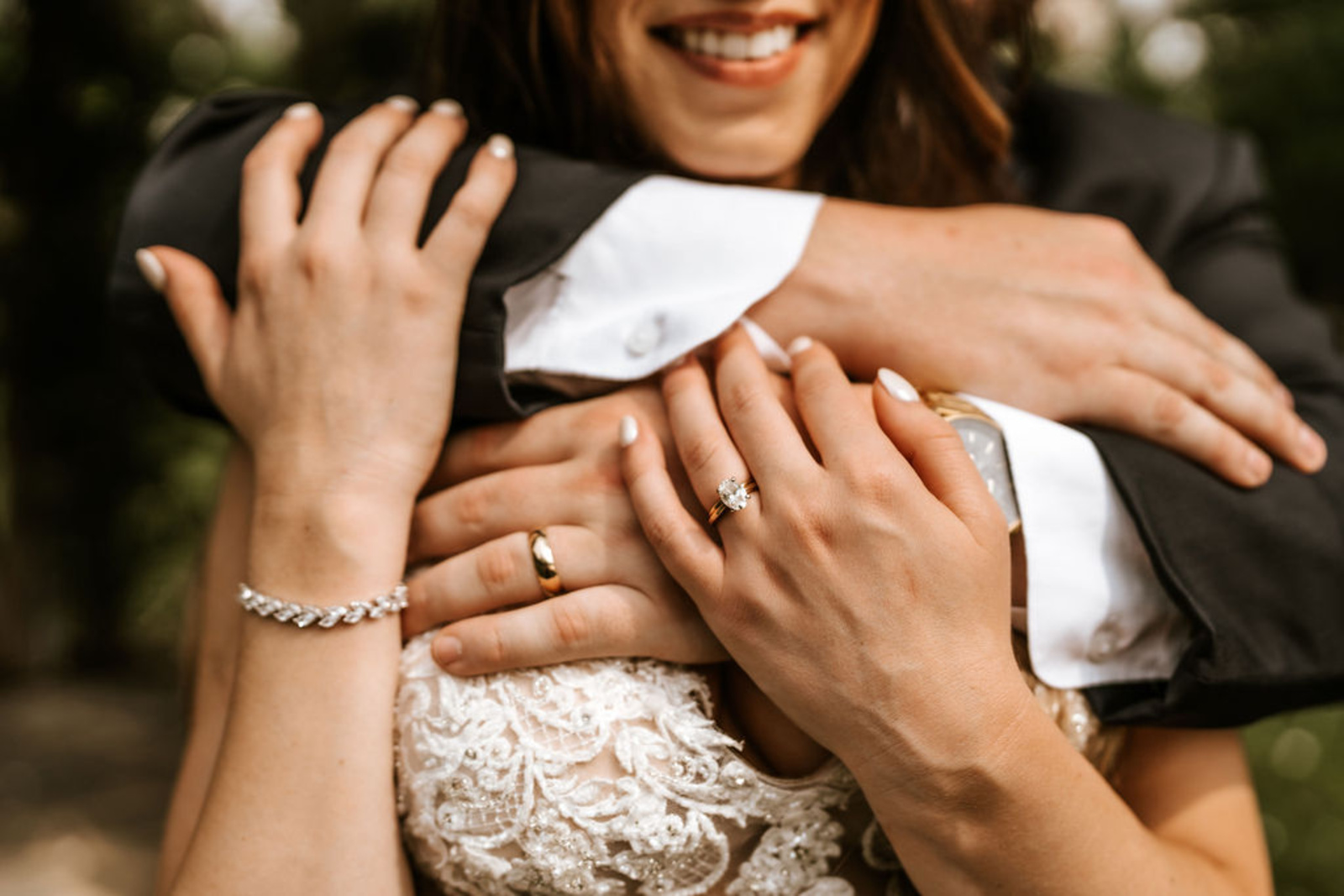 Close-up of the bride’s diamond ring and the couple’s intertwined hands as the groom embraces her during their wedding at Moonstone Manor.