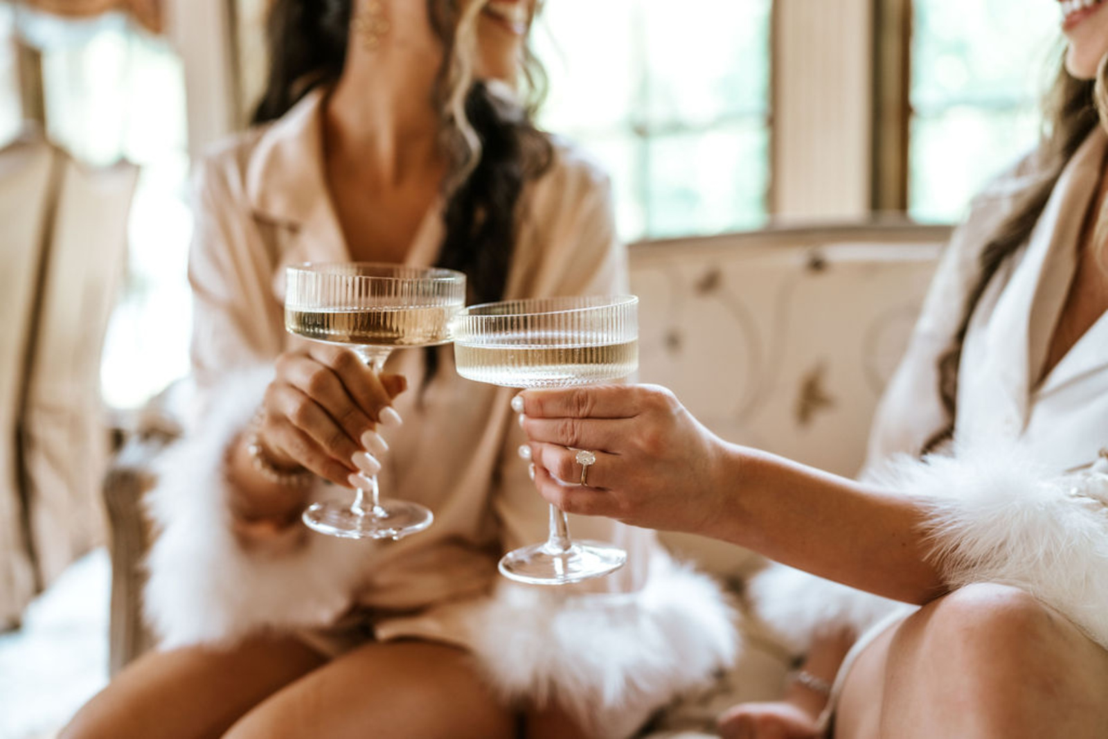 The bride and her bridesmaid in matching silk robes share a champagne toast while getting ready, celebrating the wedding morning at Moonstone Manor.