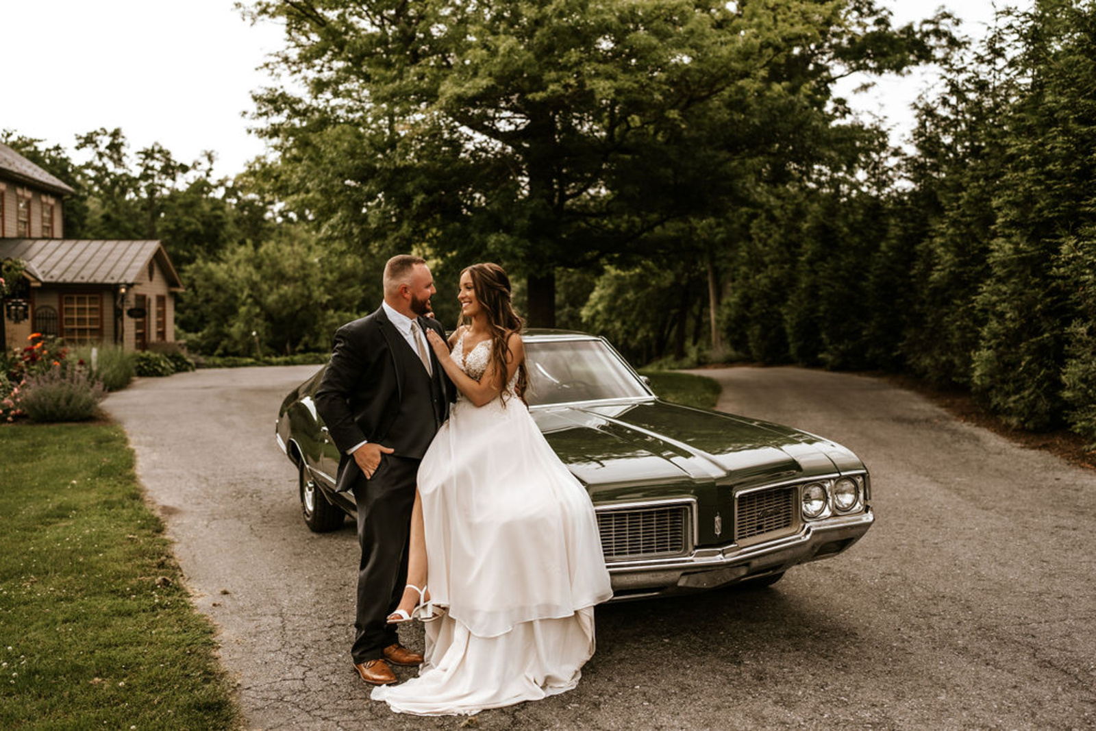 Bride and groom lean against a vintage green car in front of Moonstone Manor, sharing a joyful moment after their ceremony.