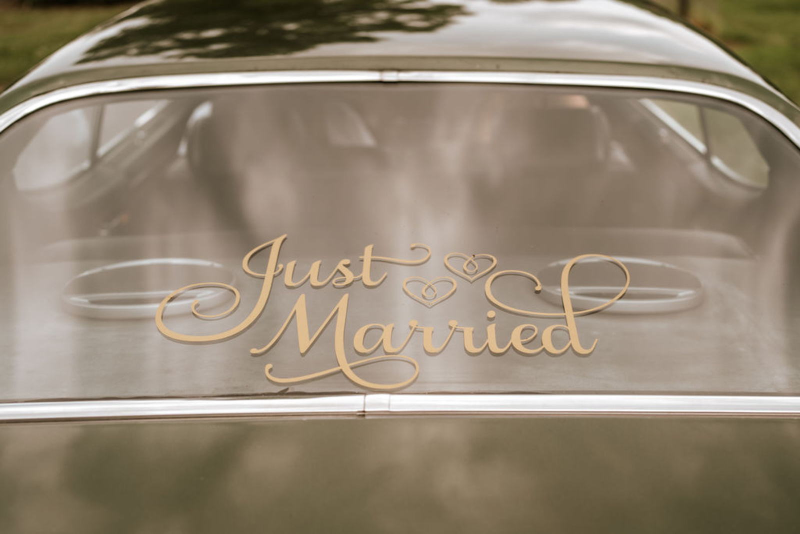 Elegant gold “Just Married” sign displayed on the rear window of the couple’s vintage car as they depart Moonstone Manor after their wedding.
