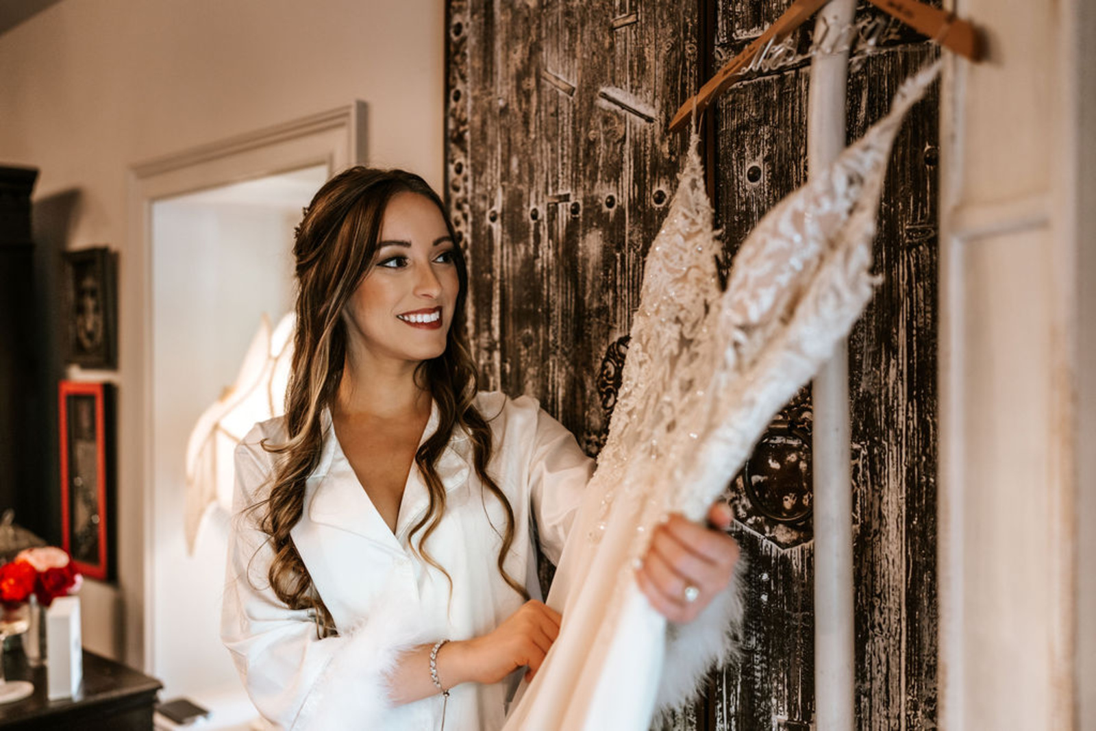 The bride smiles while holding her lace wedding dress on a custom hanger, preparing for her intimate Moonstone Manor ceremony in Central Pennsylvania.
