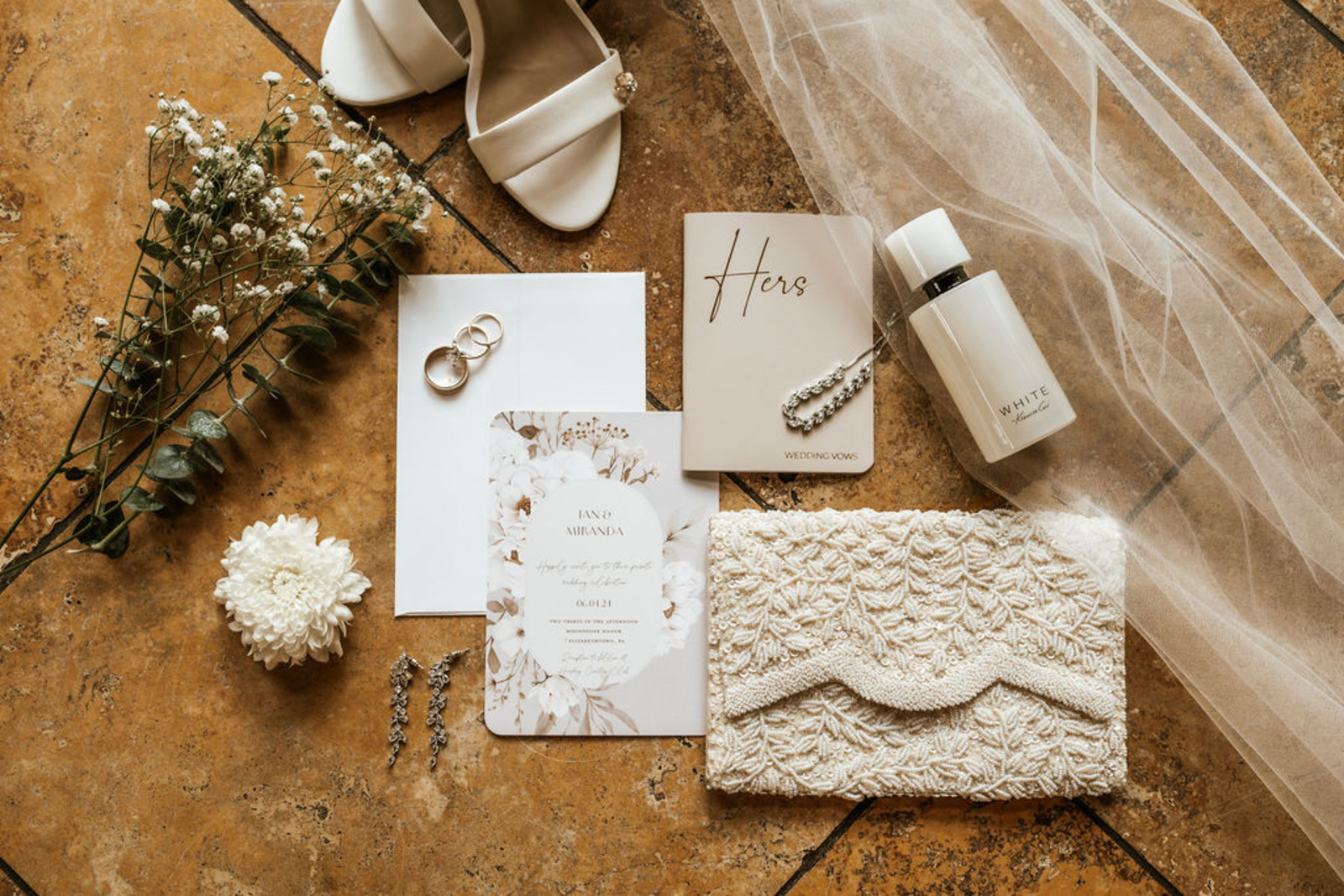 Close-up of gold wedding bands and oval-cut engagement ring displayed on a floral wedding invitation with greenery accents at Moonstone Manor in Central Pennsylvania.