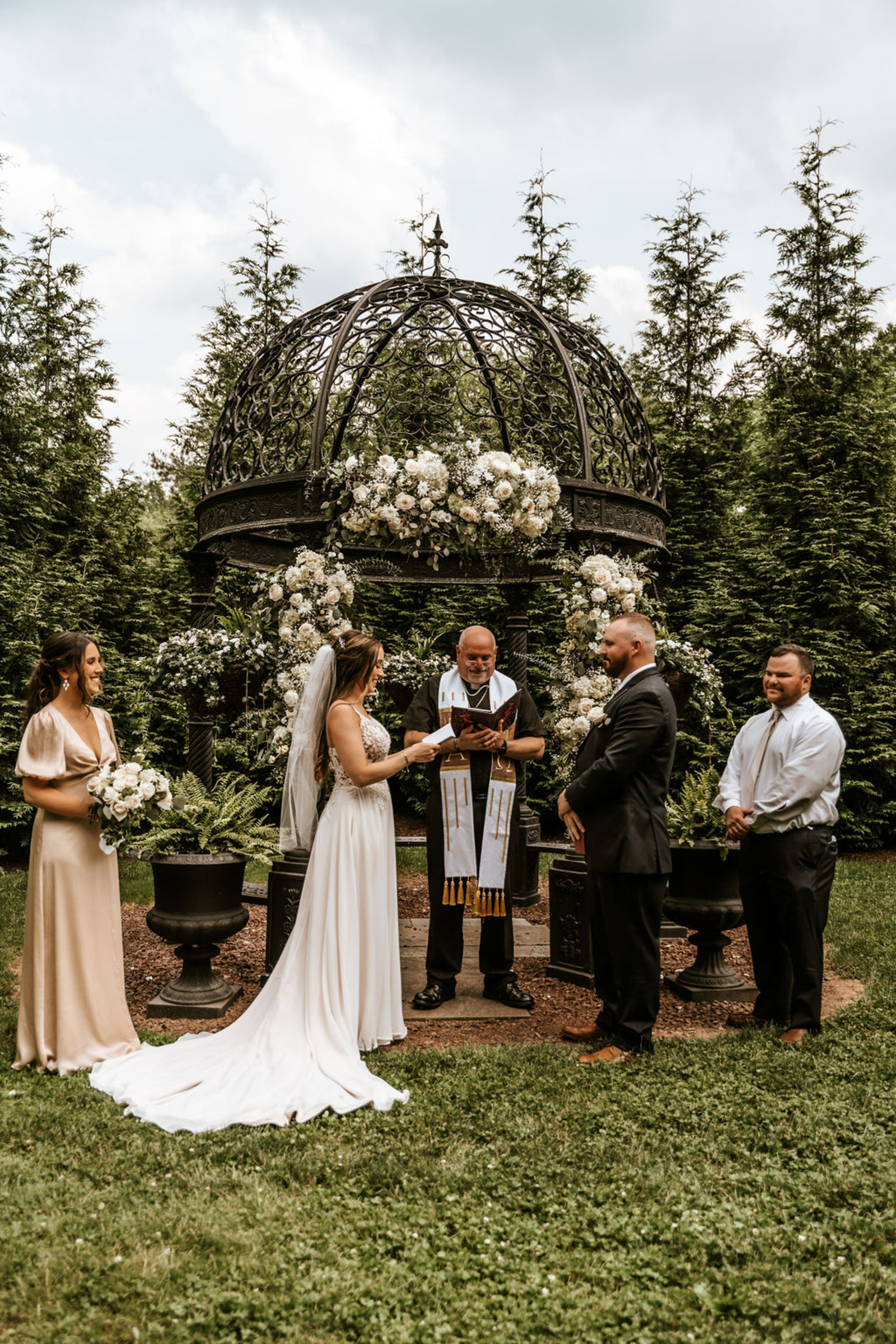The bride and groom exchange vows under a floral-filled iron gazebo surrounded by family and friends at Moonstone Manor in Central Pennsylvania.
