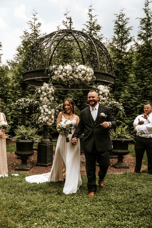 Bride and groom walking down the aisle after a garden wedding ceremony beneath an ornate gazebo with lush white floral installations in Central Pennsylvania.