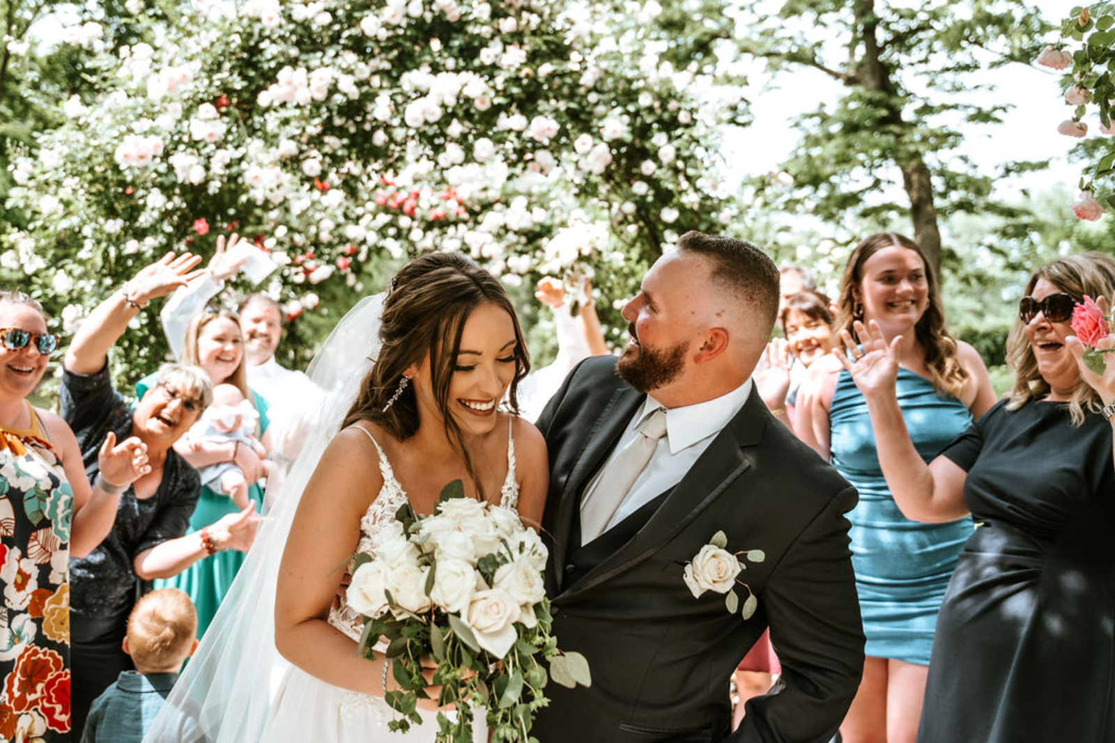 The newlyweds walk through a floral arch as guests cheer, celebrating their intimate and romantic Moonstone Manor wedding.