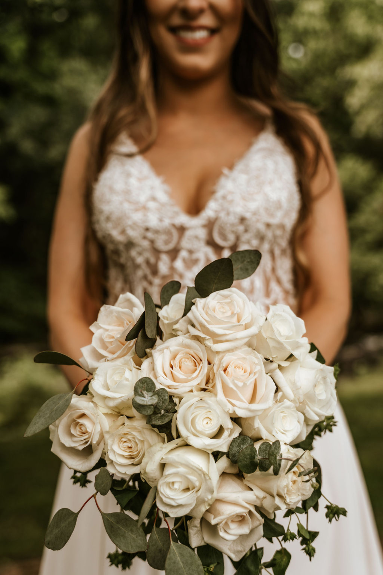 Close-up of the bride’s classic white and blush rose bouquet accented with eucalyptus, perfectly complementing her lace wedding gown.