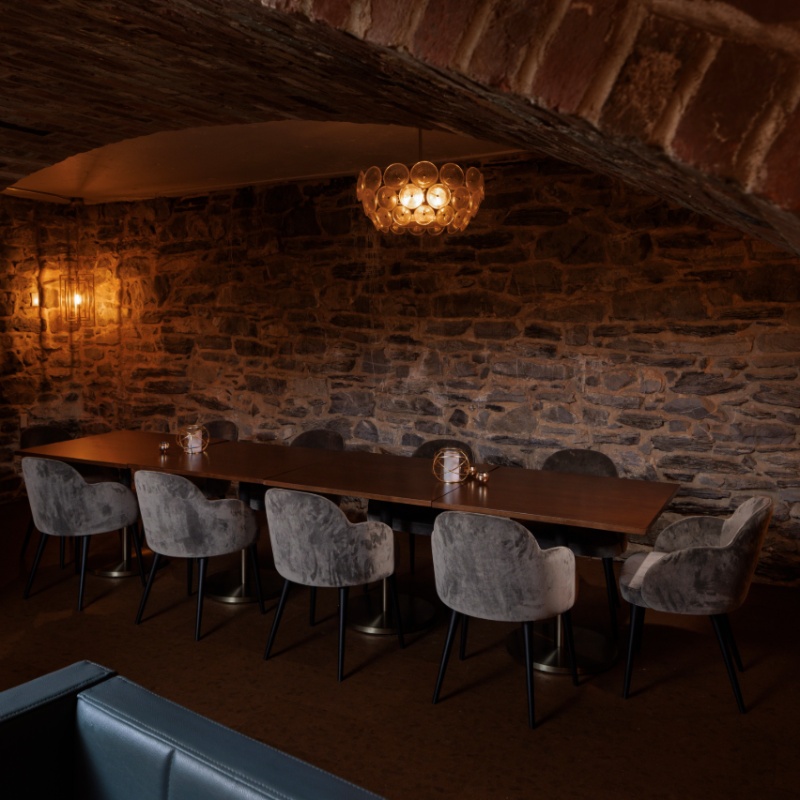 Private dining area at Proof of Lancaster with a long table, upholstered chairs, exposed stone walls, and warm ambient lighting.