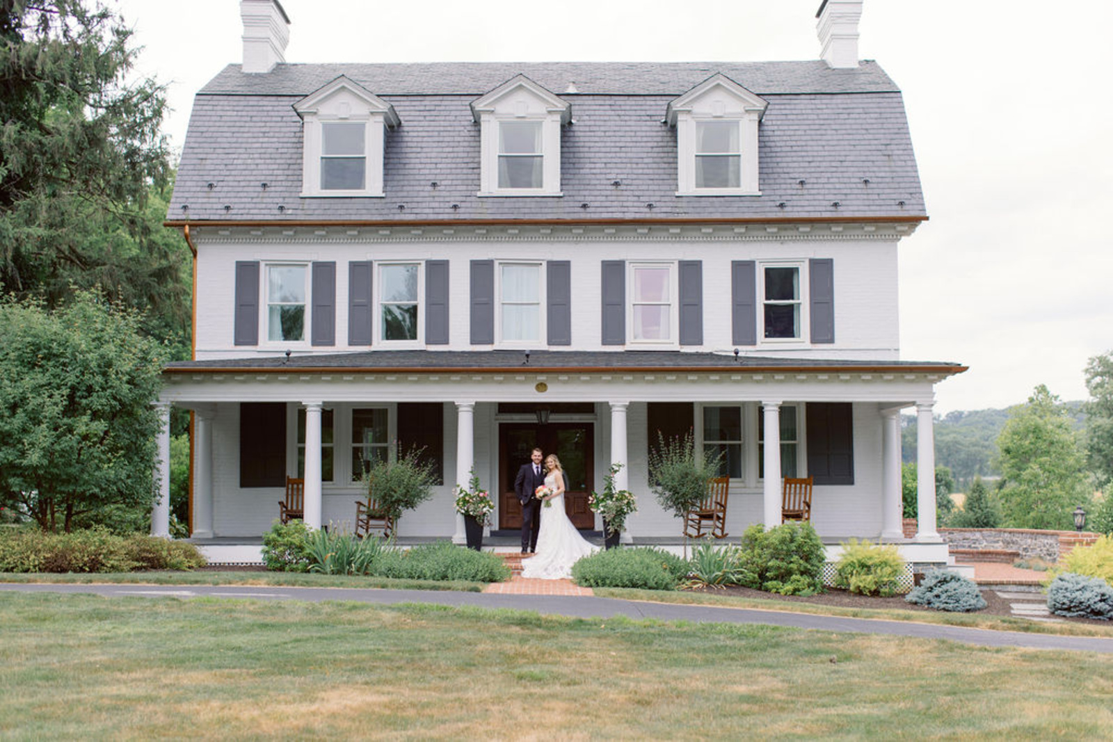 Bride and groom standing in front of Historic Ashland’s white estate home during their romantic early summer wedding in Pennsylvania.