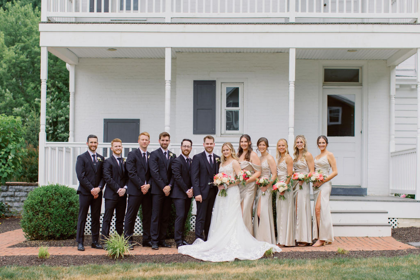 Bride and groom posing with bridesmaids in champagne dresses and groomsmen in navy tuxes outside Historic Ashland.