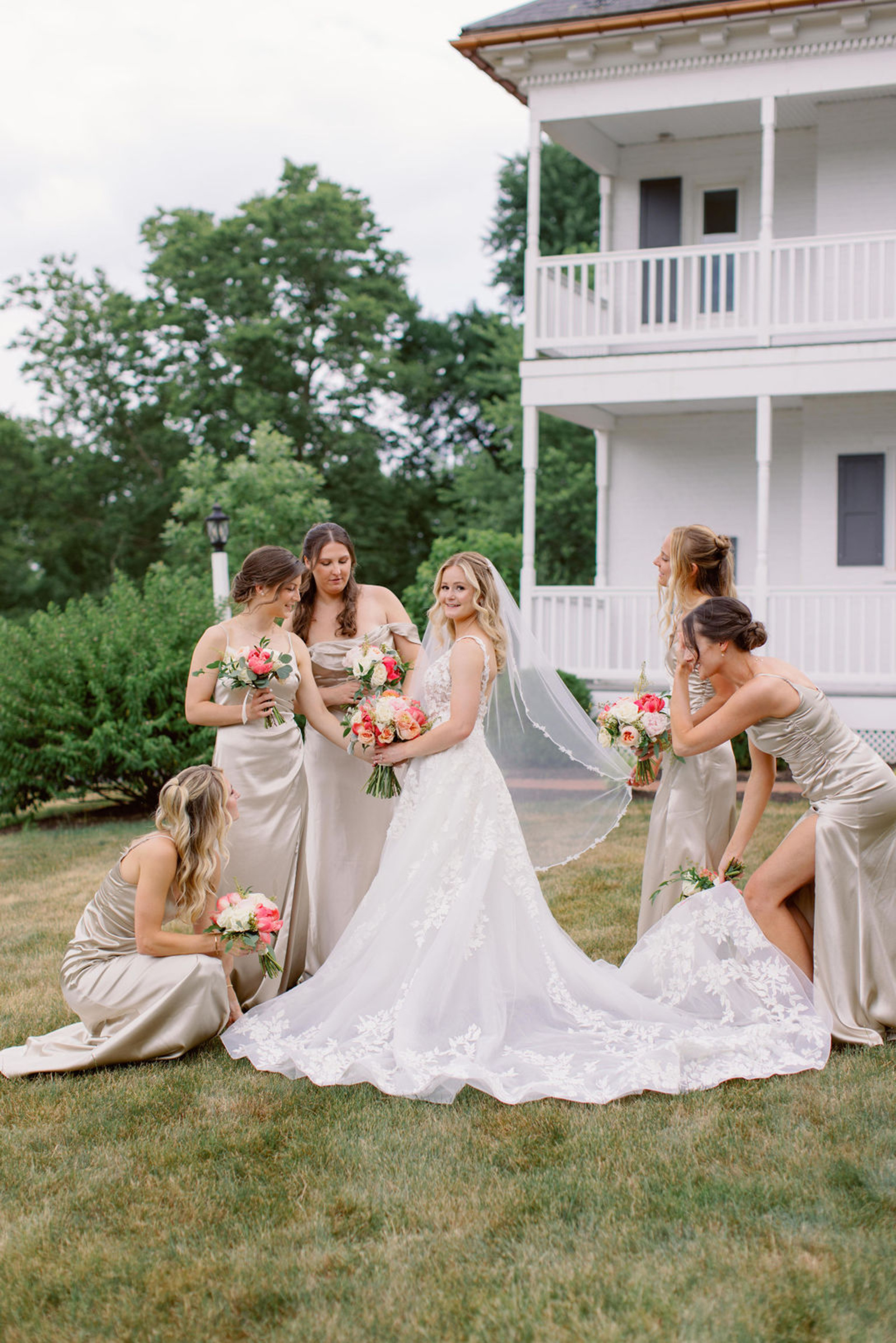 Bride posing with bridesmaids in champagne satin dresses outside Historic Ashland during an early summer wedding in Pennsylvania.