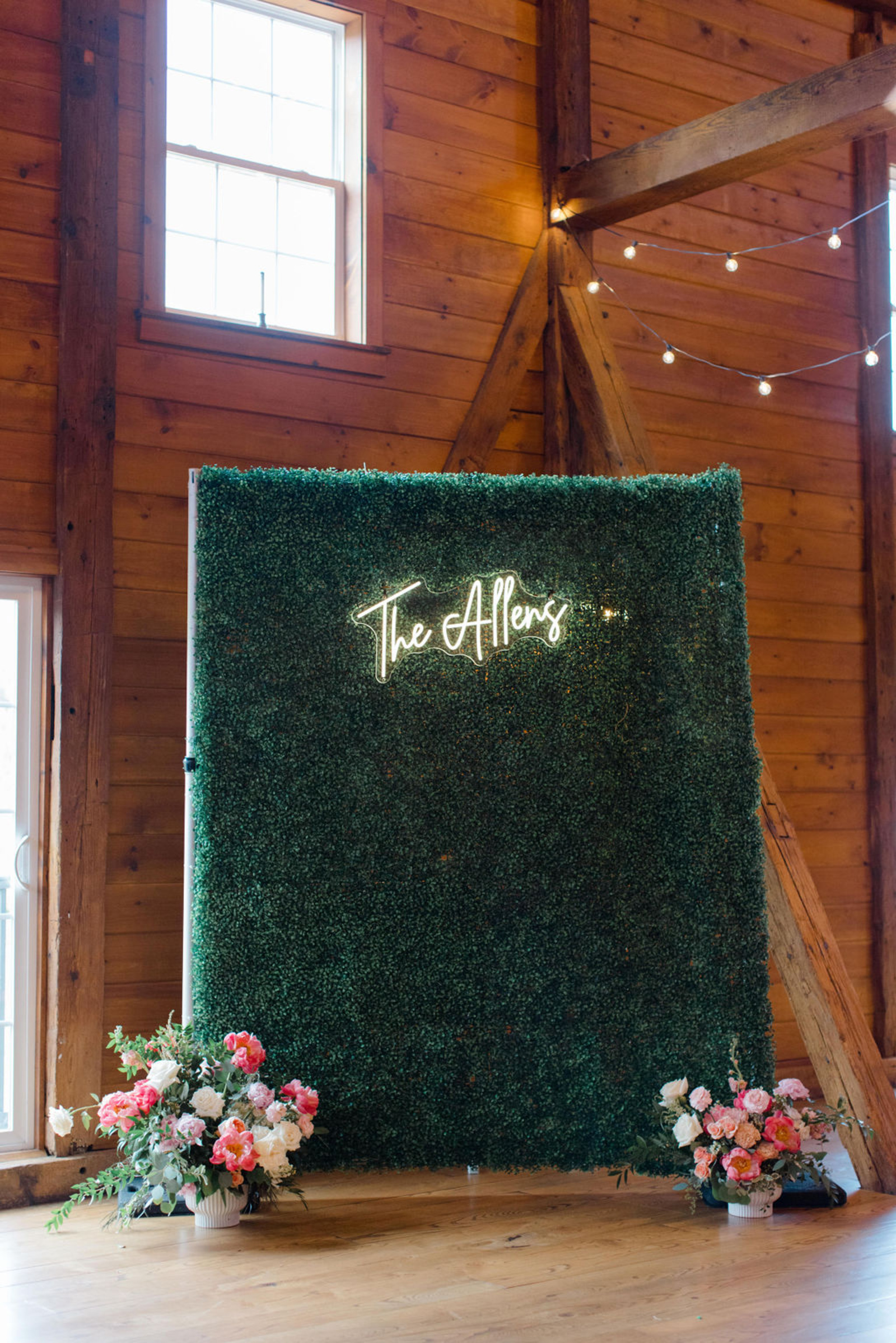 Green hedge wall with neon “The Allens” sign and bright summer florals inside Historic Ashland’s reception barn.