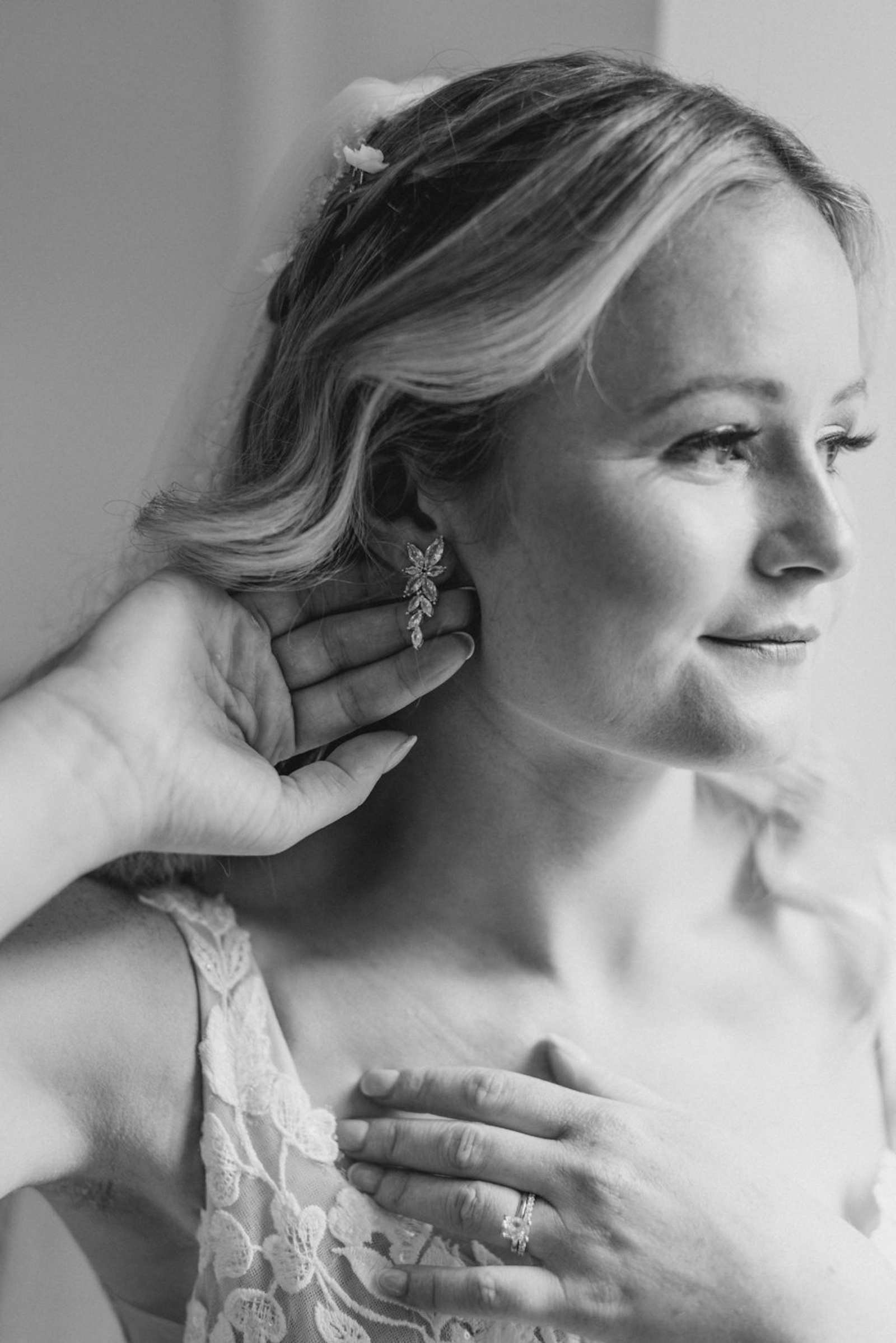 Black-and-white close-up portrait of the bride putting on floral statement earrings before her Historic Ashland wedding ceremony.