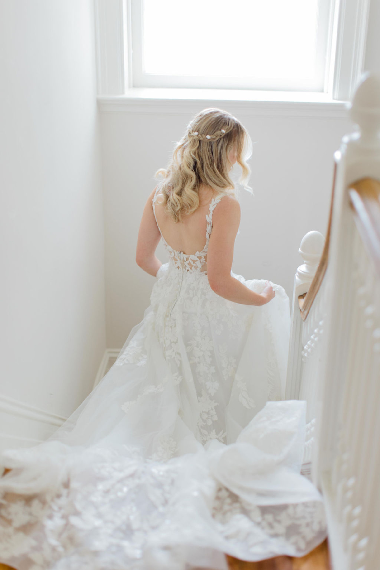Bride in a floral lace wedding gown walking down the staircase inside Historic Ashland before her early summer wedding ceremony.
