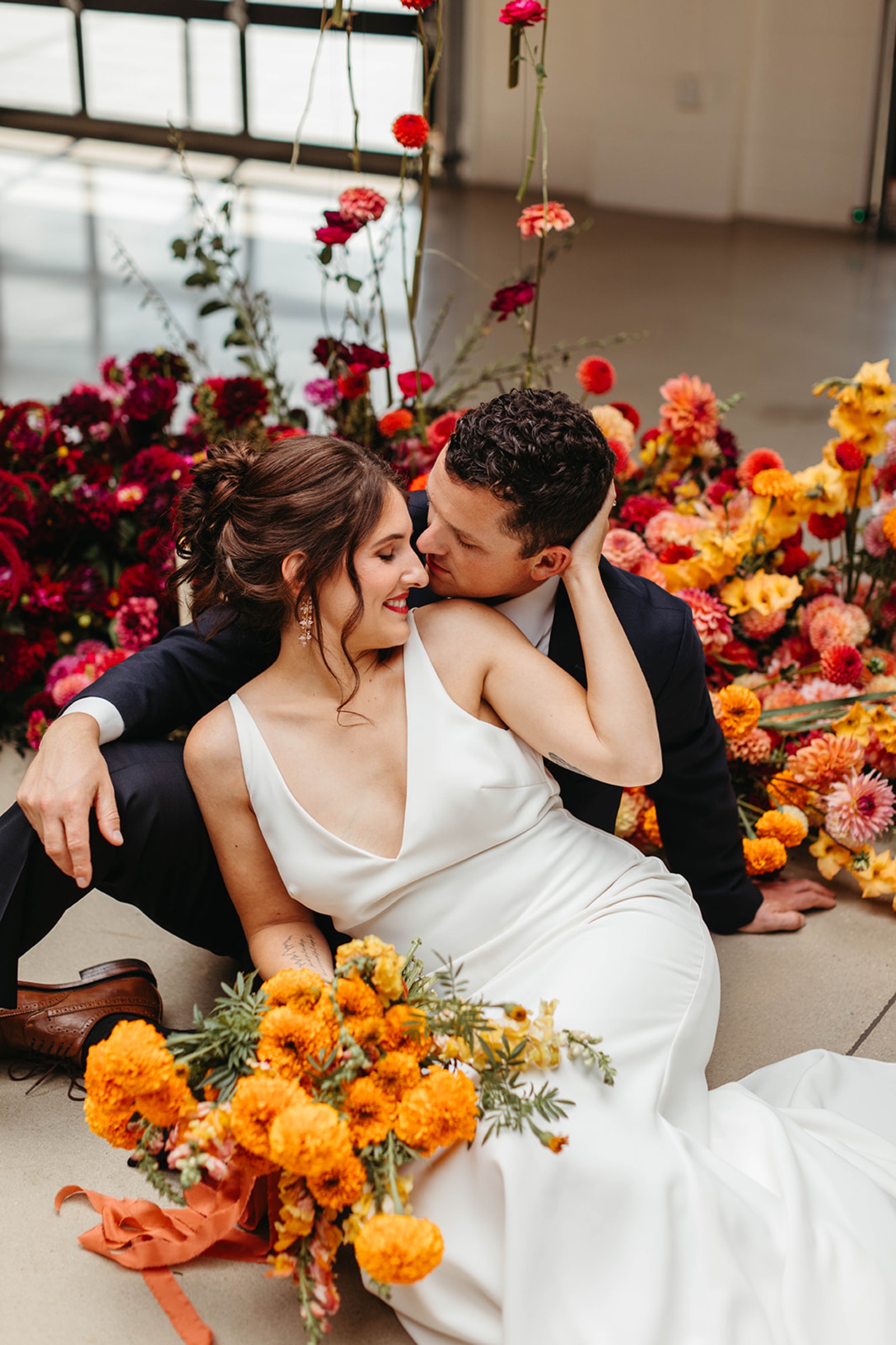 Colorful Wedding Portrait at The Booking House Bride and groom posing in front of colorful orange, pink and red wedding florals at The Booking House.