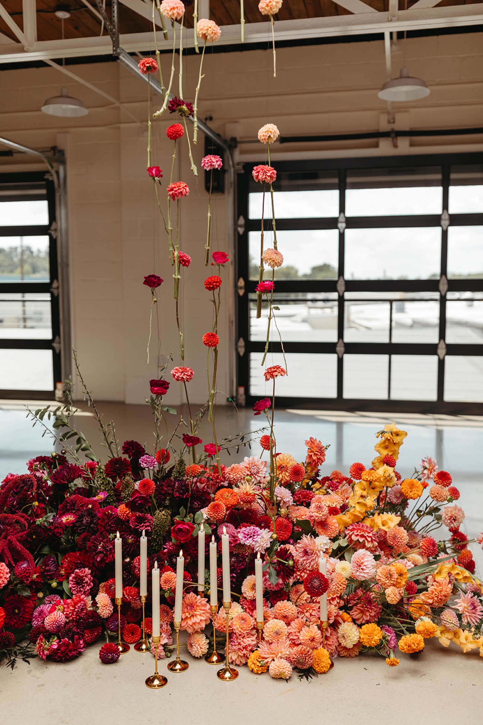 Floor-to-Ceiling Wedding Florals Hanging flowers above layered orange, pink and burgundy ceremony florals with taper candles.