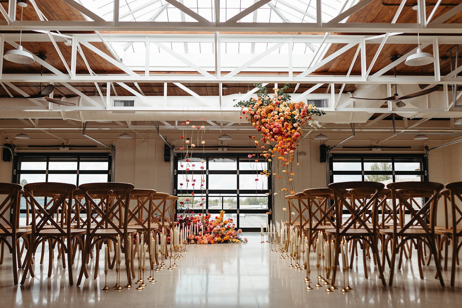 Colorful Wedding Ceremony at The Booking House Wide view of a colorful wedding ceremony setup at The Booking House with suspended florals, wooden chairs and taper candles.