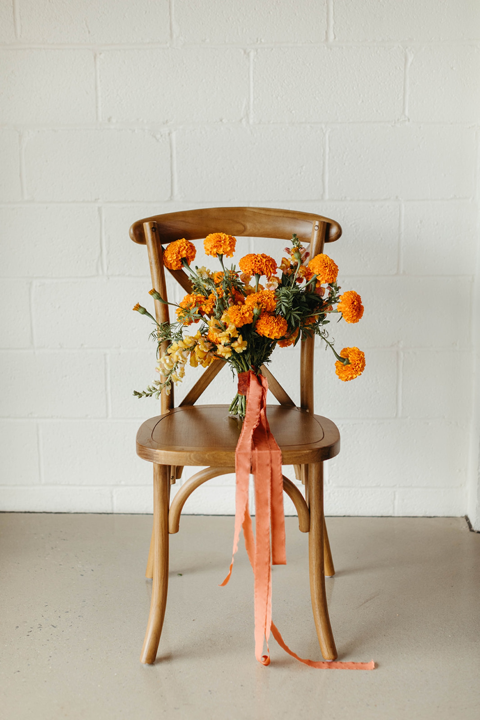 Orange Wedding Bouquet Inspiration Orange wedding bouquet with long rust-colored ribbon displayed on a wooden chair.