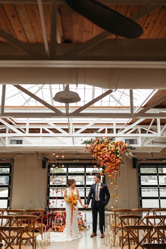 Dramatic hanging floral installation with bold orange and warm-toned blooms inside a modern wedding venue, highlighting statement floral trends for 2026 weddings.