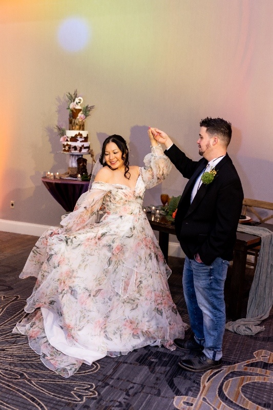 Bride and Groom Dance at Oklahoma!-Inspired Wedding The bride twirls in a flowing floral gown while the groom in a casual western look smiles beside her, surrounded by rustic décor and warm lighting inspired by Oklahoma!.