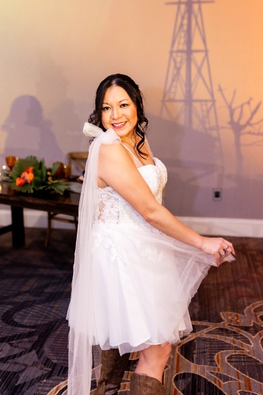 Bride in Short Lace Dress and Cowboy Boots A bride smiles in a short lace wedding dress paired with a long veil and cowboy boots, embodying playful country charm in this Oklahoma!-inspired styled shoot.