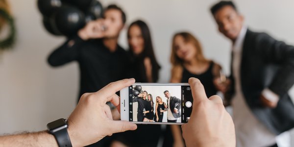 Guests taking candid photos together during a wedding or celebration while someone snaps a group picture on a smartphone, highlighting the kind of real-time guest memories couples can easily collect and share through a wedding QR code experience.