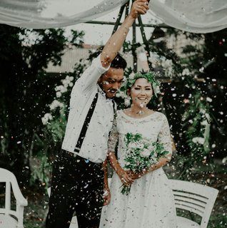 Newlywed couple celebrating outdoors under a white canopy with confetti falling around them.
