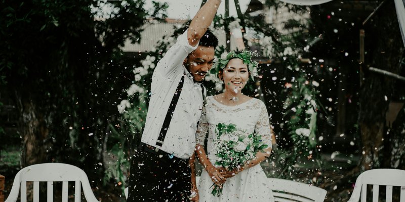 Newlywed couple celebrating outdoors under a white canopy with confetti falling around them.
