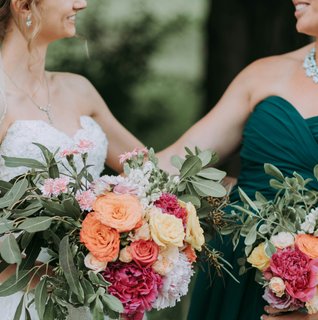 Bride and her maid of honor smiling together while holding colorful bouquets during an outdoor wedding in Central Pennsylvania.