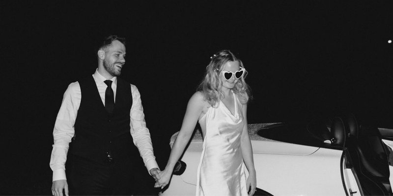 Bride and groom holding hands beside a white convertible at night, with the bride wearing heart-shaped sunglasses and a satin reception dress during a romantic Pennsylvania wedding reception sendoff.