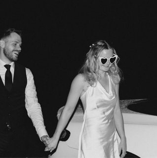 Bride and groom holding hands beside a white convertible at night, with the bride wearing heart-shaped sunglasses and a satin reception dress during a romantic Pennsylvania wedding reception sendoff.