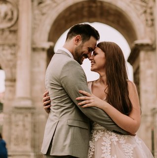 Romantic couple embracing beneath historic European-style stone arches during an intimate destination wedding portrait session, with soft natural light and warm neutral tones.